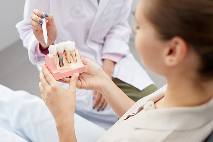 A dentist pointing to a dental implant model held by a patient