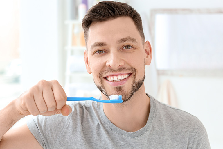 Smiling man in grey shirt about to brush his teeth