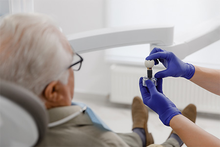 Male dental patient looking at dental implant held by dentist