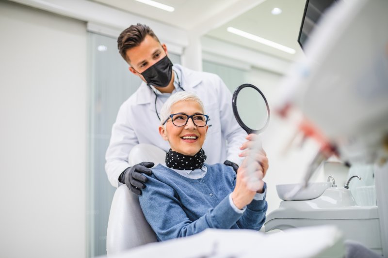 Patient smiling in mirror as she admires her new dental implants