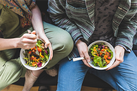 Two people holding bowls of salad in their laps