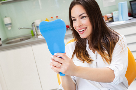 Woman sitting in dental chair holding mirror