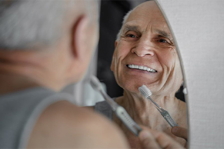 Man smiling while brushing his teeth in the mirror