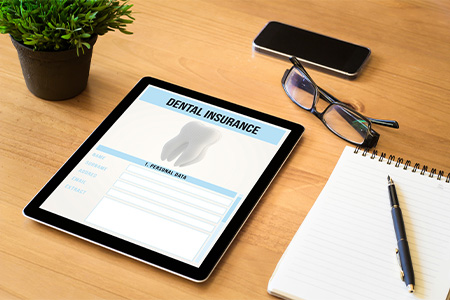Tablet with dental insurance form lying next to glasses, notepad, and phone