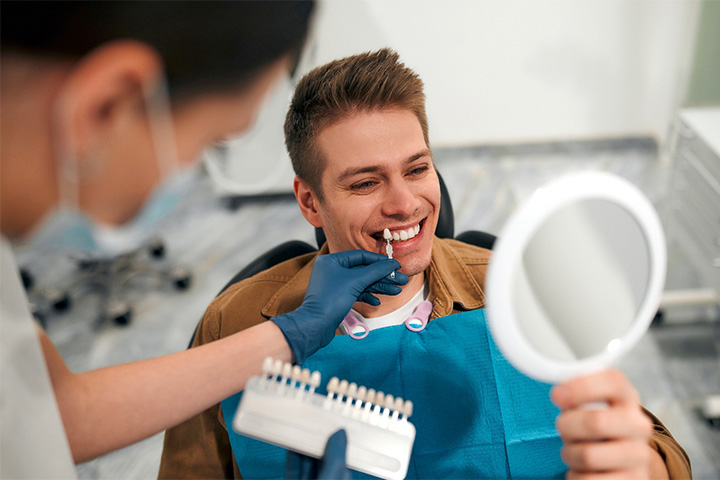 A cosmetic dentist holding a shade chart up to a patient’s smile