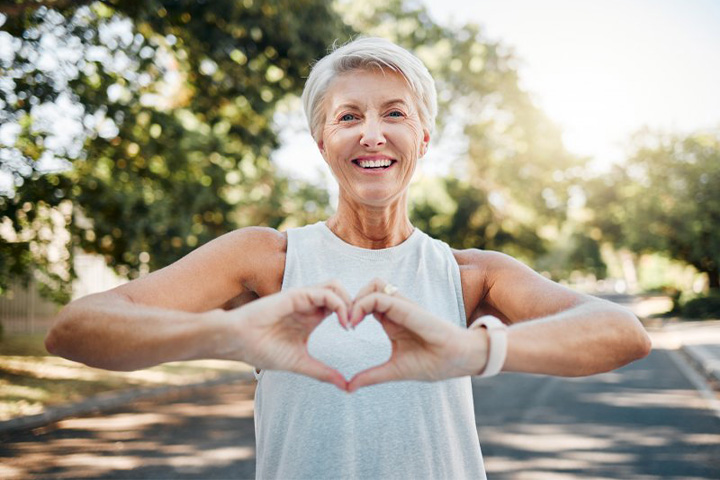 Lady smiles while making shape of heart with hands.