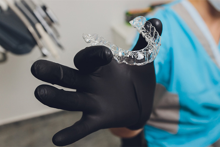 Dentist with black gloved hand holding an Invisalign aligner.