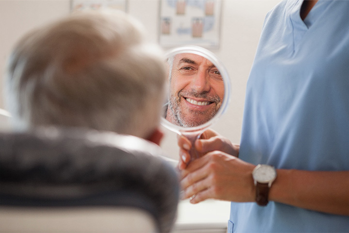 Man smiling at reflection in handheld mirror.