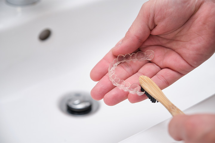 Person cleaning their Invisalign with a toothbrush.
