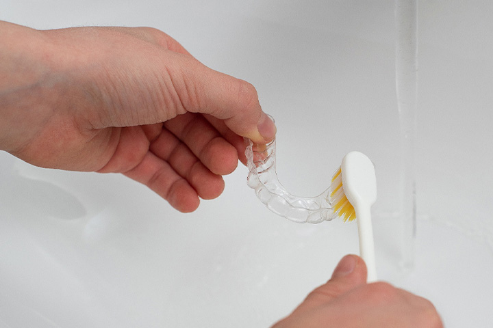 Person using a toothbrush to scrub their aligner.