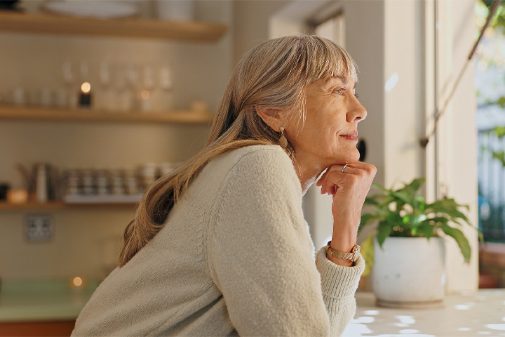 Senior woman smiling while looking out the window at home.